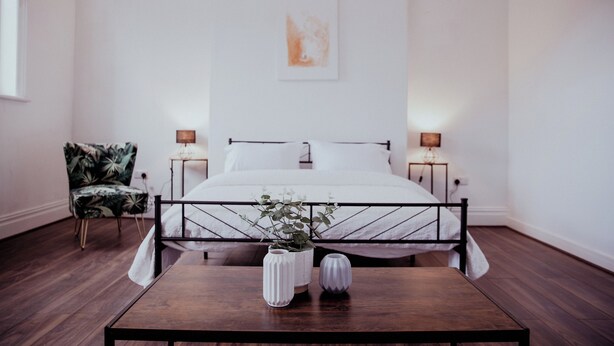 Une chambre à coucher avec un lit, des tables de chevet, une chaise et une table ornée de vases.