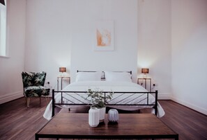 A bedroom with a bed, bedside tables, a chair, and a table with vases. - Holmfirth converted bank: centre of Town (Holmfirth)
