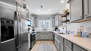 A modern kitchen with stainless steel appliances, grey cabinets, a large window, and a blue patterned rug. - ⭐Private Pool-4 Bikes-30A-Beach Access-Claddagh Cottage⭐ (Santa Rosa Beach)