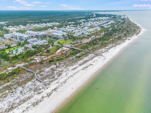 Vue aérienne d’une zone résidentielle côtière, avec des maisons, une plage et un pont.