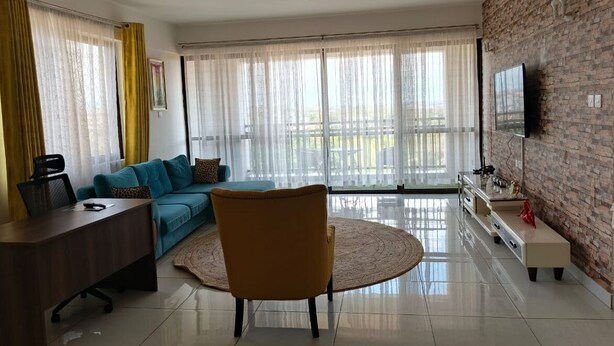 Una sala moderna con un sofá, un sillón amarillo, un televisor y un ventanal con cortinas.