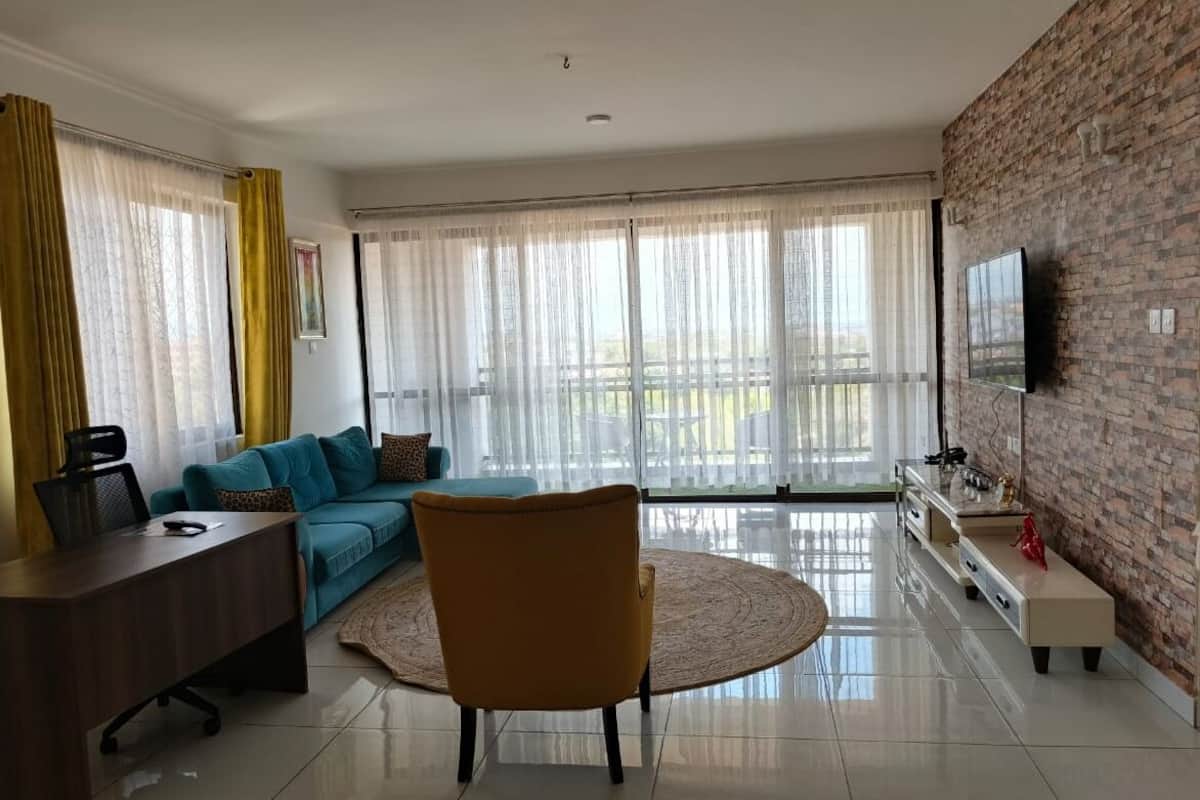 A modern living room with a sofa, a yellow chair, a TV, and a large window with curtains.