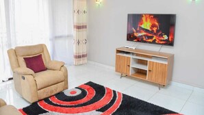 Una sala de estar con un sofá color beige, un televisor en la pared, un mueble de madera y una cortina a rayas.