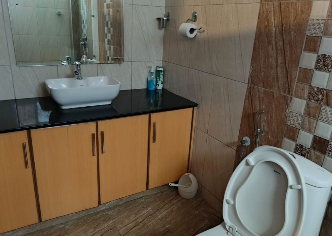 Une salle de bain avec un lavabo blanc, des meubles en bois, des toilettes et un miroir.