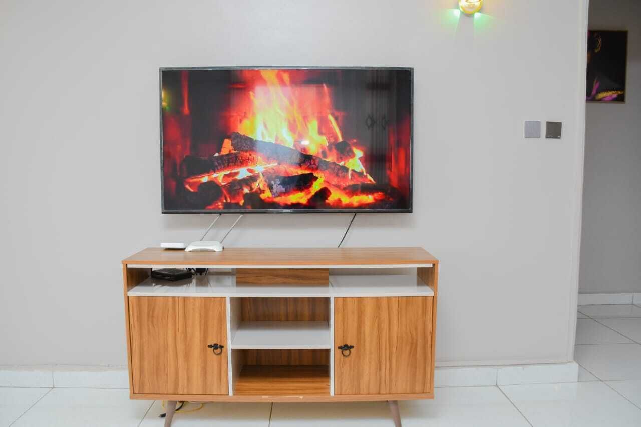 A flat-screen TV mounted on a wall above a wooden TV stand with open shelves.
