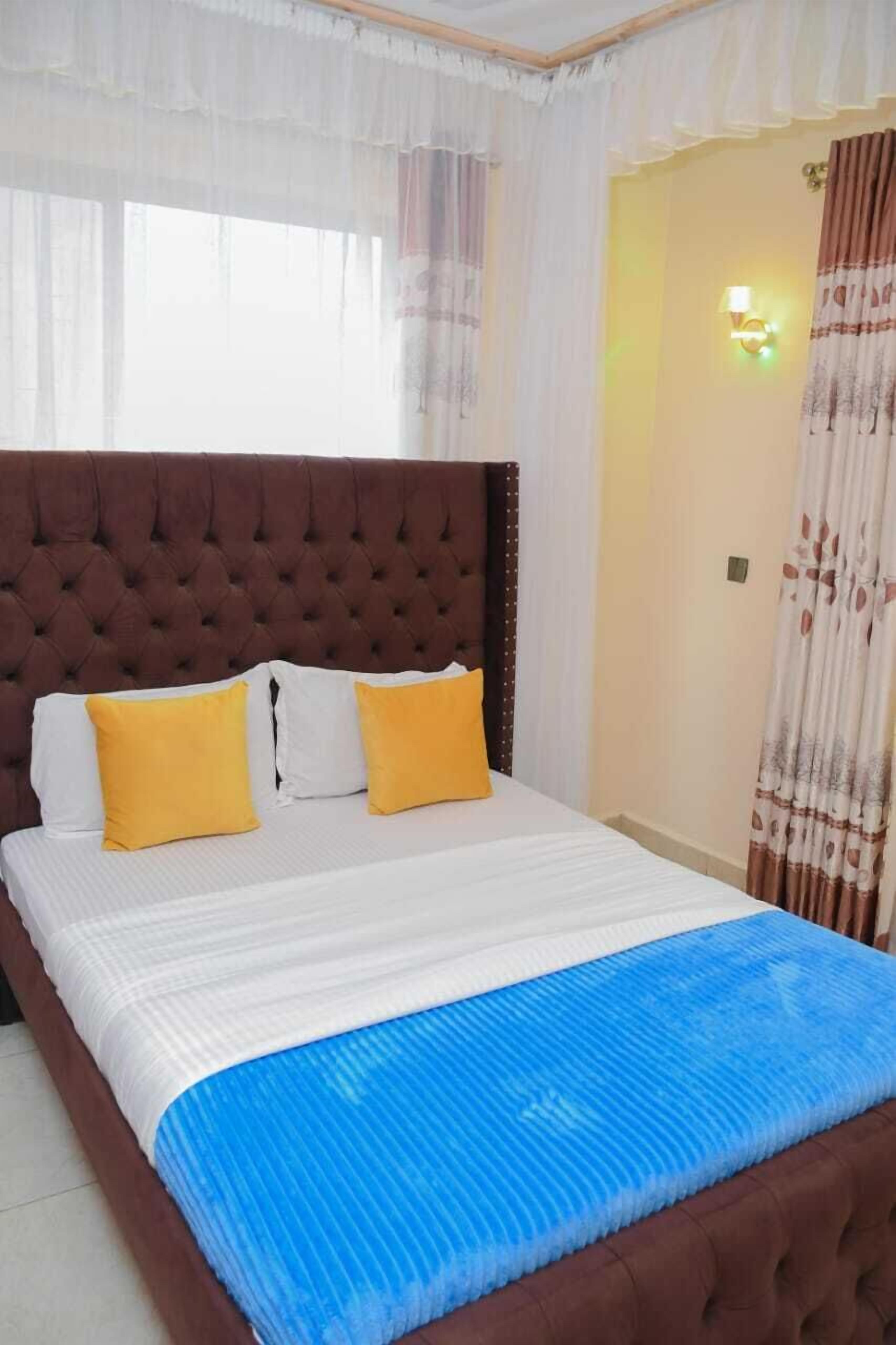 A bedroom with a tufted headboard, a bed with white and yellow pillows, and a blue bedspread.