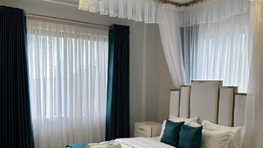 Un dormitorio moderno con una cama grande, cortinas blancas, una alfombra mullida e iluminación en el techo.