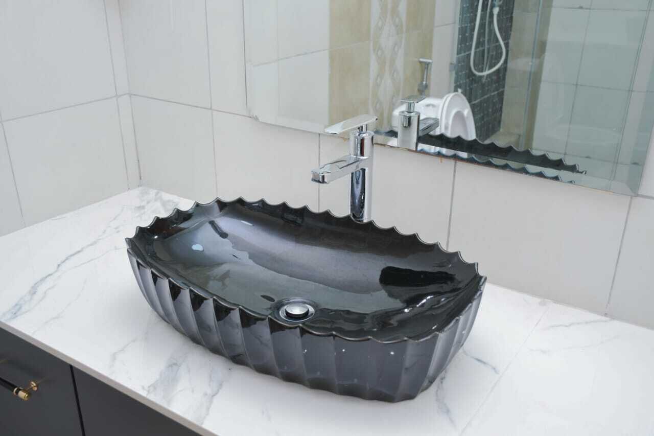 Un bagno con un lavabo nero a incasso, uno specchio e una doccia.