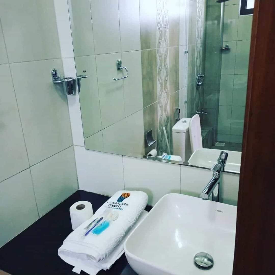 A bathroom with a white sink, a mirror, and a toilet. There is a towel and a bottle of hand soap on the counter.
