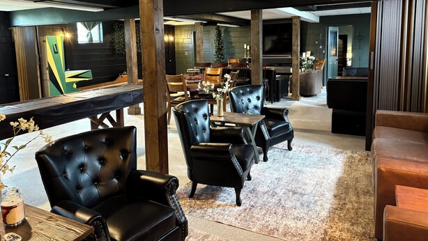 A modern lounge area with leather seating, a wooden bar, and a large flat-screen TV. - Underground Speakeasy Experience in Historic Fort Recovery - Sleeps 14 (Fort Recovery)