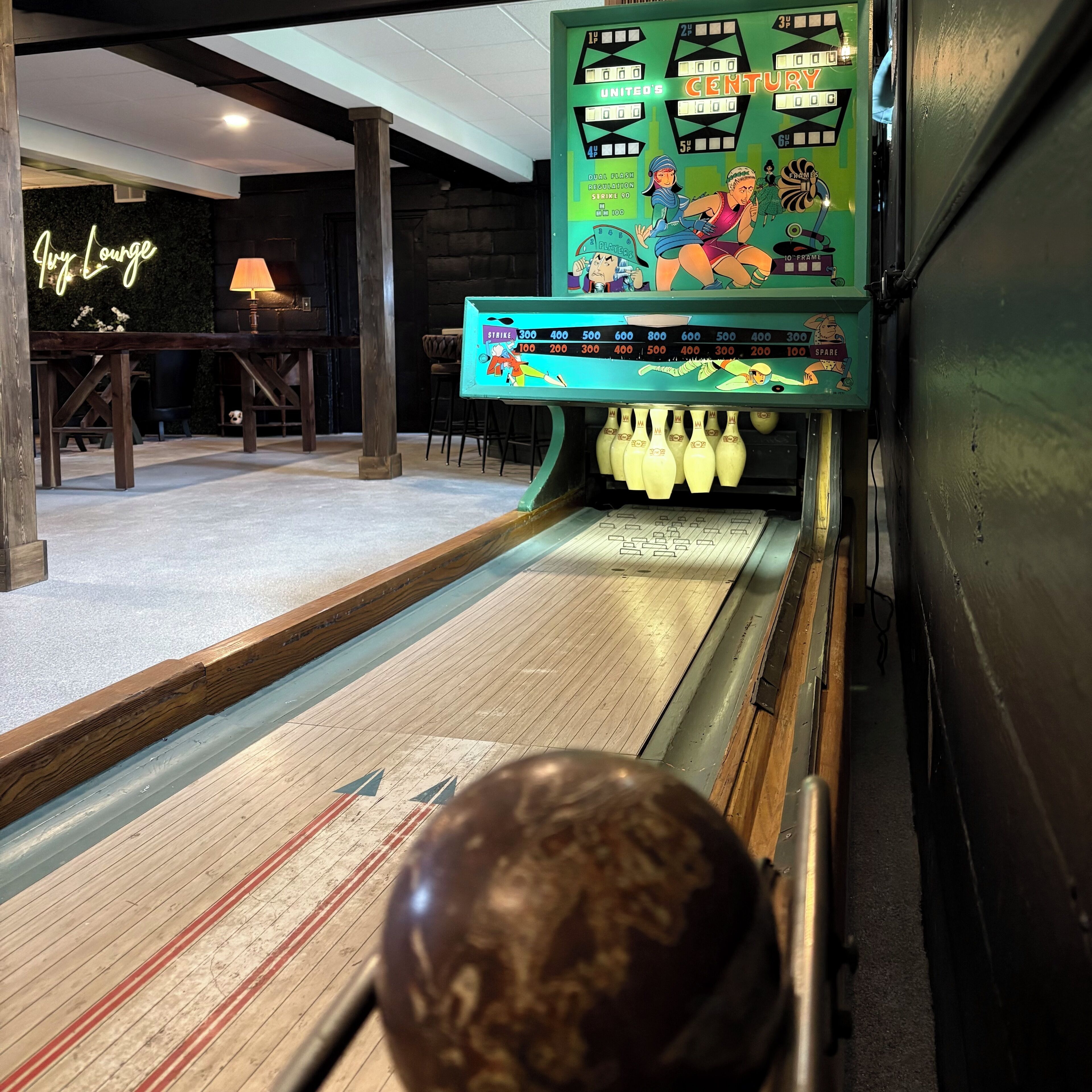 Un bowling avec une enseigne au néon indiquant « Jury Lounge », ainsi qu’une piste de bowling avec des quilles et une boule de bowling.