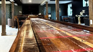 A long wooden table with red and yellow tape, set in a modern room with dark walls and a large window. - Underground Speakeasy Experience in Historic Fort Recovery - Sleeps 14 (Fort Recovery)