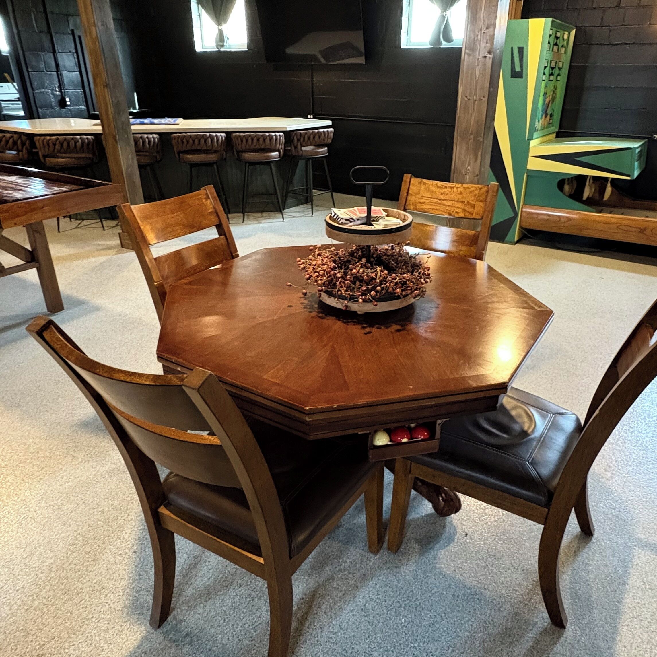 Een houten eettafel met zes stoelen, een decoratief middelpunt en een groene kast op de achtergrond.