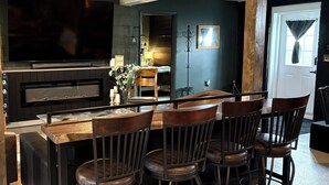 A modern kitchen with a large TV, dark cabinetry, and a bar area with stools. - Underground Speakeasy Experience in Historic Fort Recovery - Sleeps 14 (Fort Recovery)