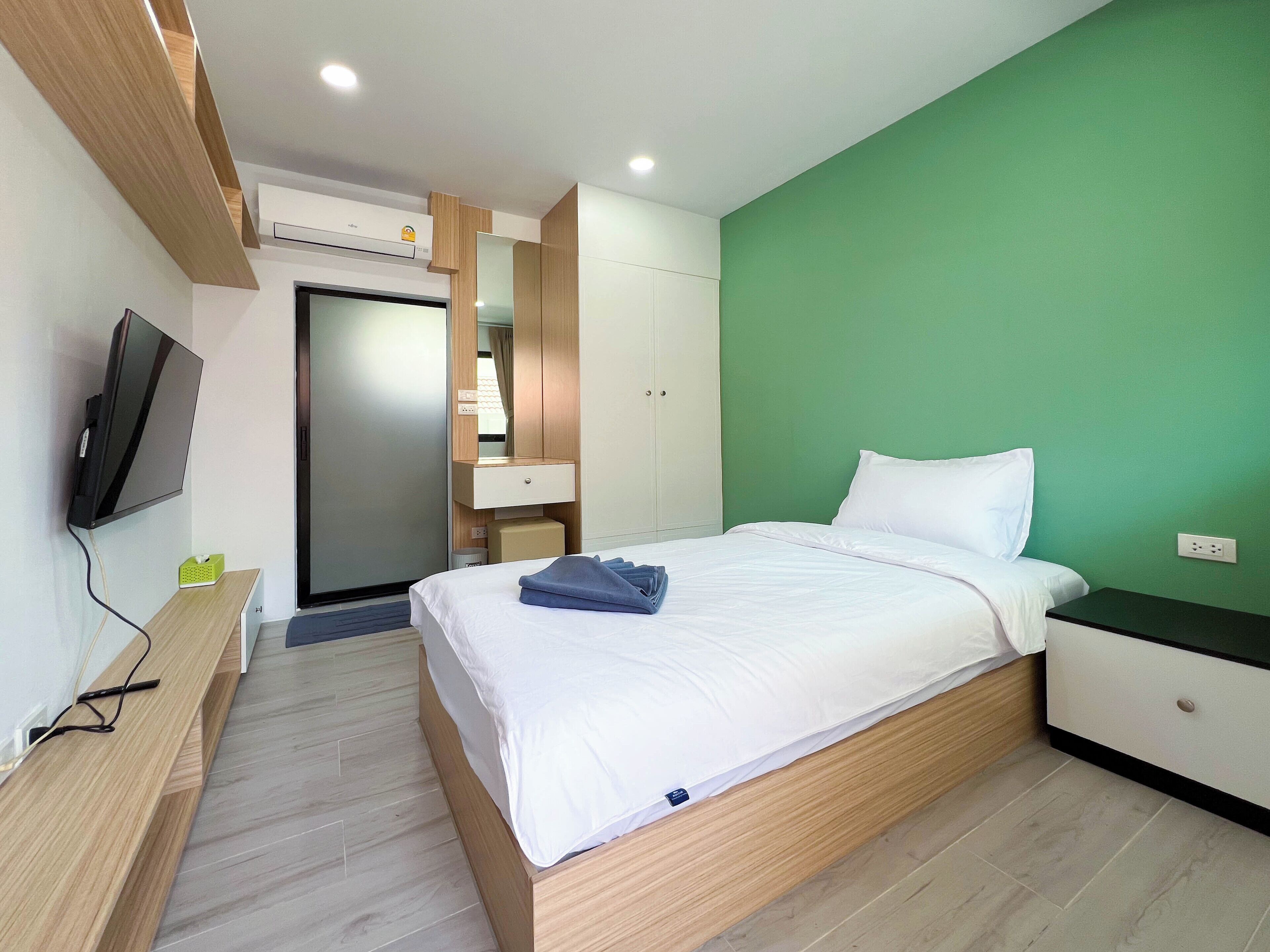 A modern hotel room with a bed, bedside table, TV, and a green accent wall.