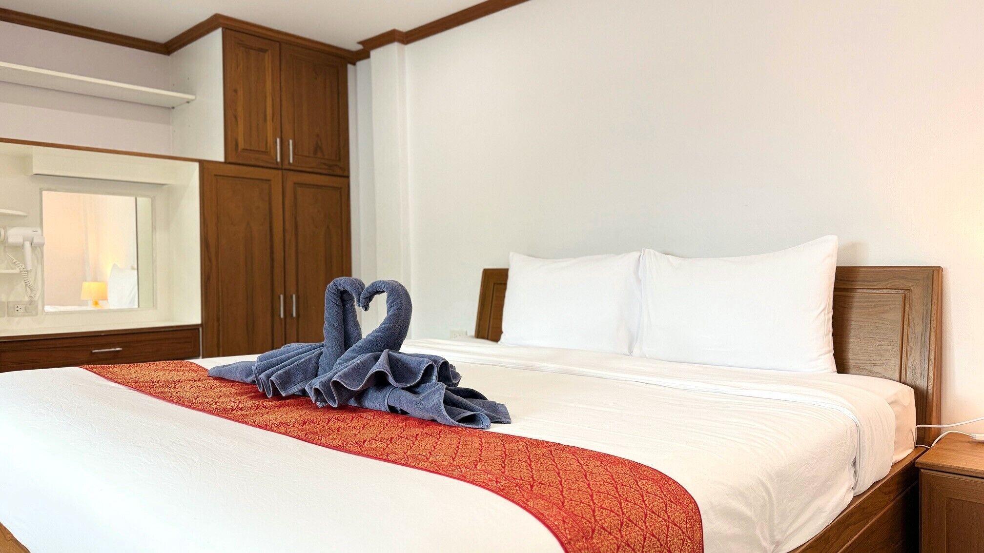 Una habitación de hotel con una cama bien hecha, un plaid rojo y blanco estampado y una toalla dispuesta en forma de corazón sobre la cama.