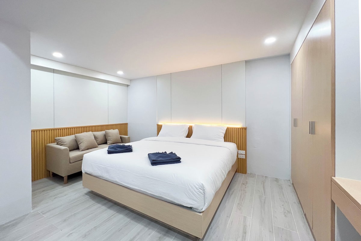 Moderni hotellihuone, jossa on suuri sänky, sohva ja vaatekaappi.