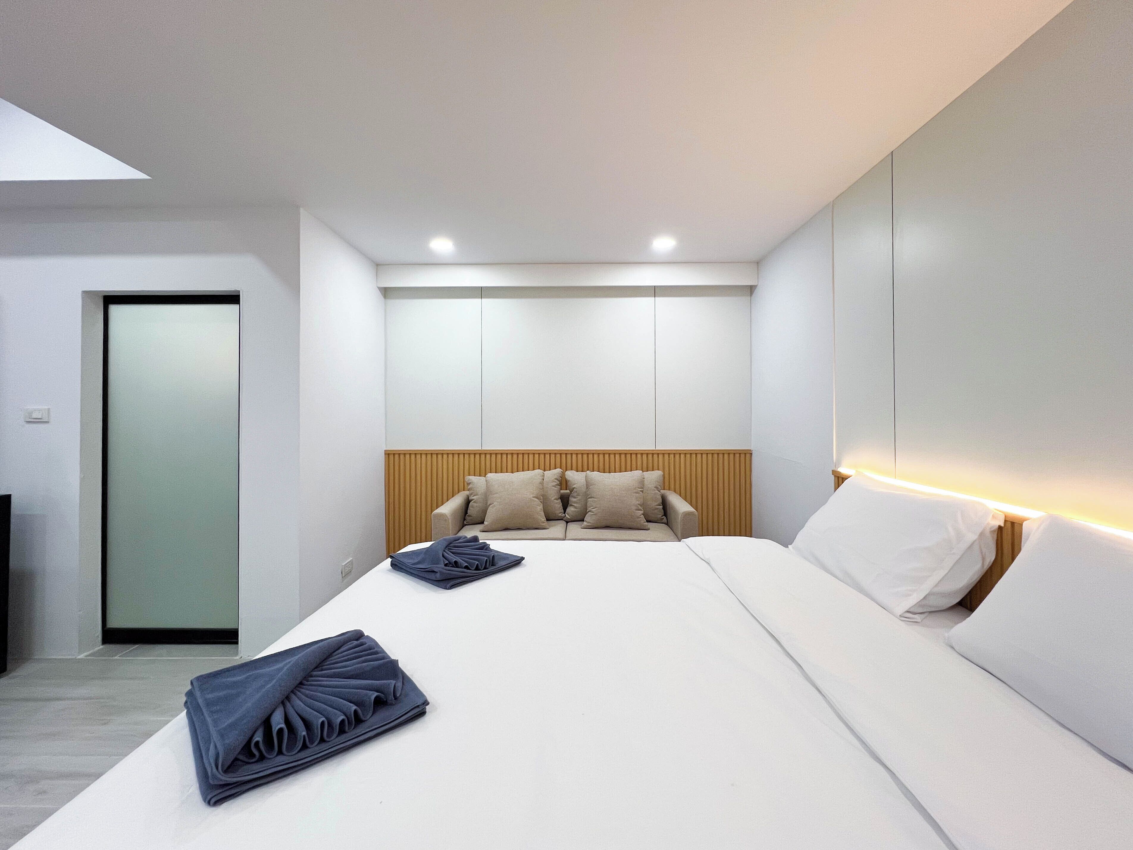 A modern hotel room with a bed, a wooden headboard, and a large window.