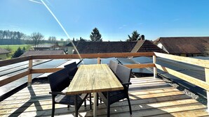Una terraza de madera con una mesa y sillas, que da vista a una zona residencial con casas y árboles.