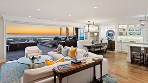 A spacious living area with a large window overlooking a beach, furnished with a sofa, coffee table, and dining area. - Seacliff Beach Retreat Amazing Beachfront for 6 (Ventura)