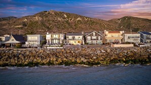 A coastal hotel with a stone wall and multiple buildings along the shore, overlooking a mountainous landscape. - Seacliff Beach Retreat Amazing Beachfront for 6 (Ventura)