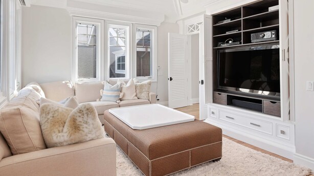 Ein Wohnzimmer mit einem beige-farbenen Sofa, einem weißen Couchtisch und einem großen Flachbildfernseher auf einer weißen Unterhaltungseinheit.