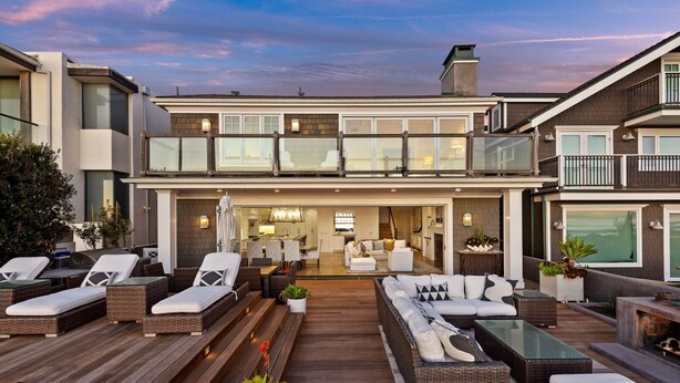 A modern two-story house with a spacious outdoor patio area featuring wicker furniture, a dining area, and a kitchen visible through large windows. - Seacliff Beach Retreat Amazing Beachfront for 6 (Ventura)