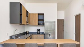 Una cocina moderna con encimera de madera, cuatro sillas grises, un refrigerador de acero inoxidable y una cafetera.