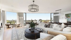 A spacious living area with a large window, a round coffee table, and a modern chandelier. - Luxury Villas Como Penthouse (Melbourne skyline and river views) (South Yarra)