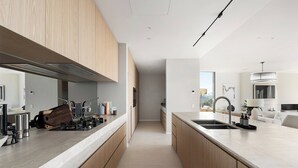 A modern kitchen with a long island, stainless steel appliances, and wooden cabinets. - Luxury Villas Como Penthouse (Melbourne skyline and river views) (South Yarra)