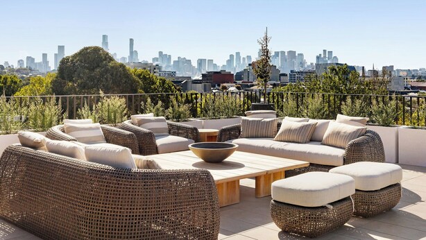A rooftop terrace with wicker furniture, a round table, and a city skyline view. - Luxury Villas Como Penthouse (Melbourne skyline and river views) (South Yarra)