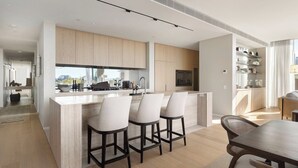A modern kitchen with a central island, bar stools, and a dining area with a wooden table. - Luxury Villas Como Penthouse (Melbourne skyline and river views) (South Yarra)