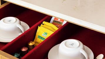 A kitchen counter with a coffee maker, a kettle, and a drawer containing cups, a spoon, and a packet of honey ginger.