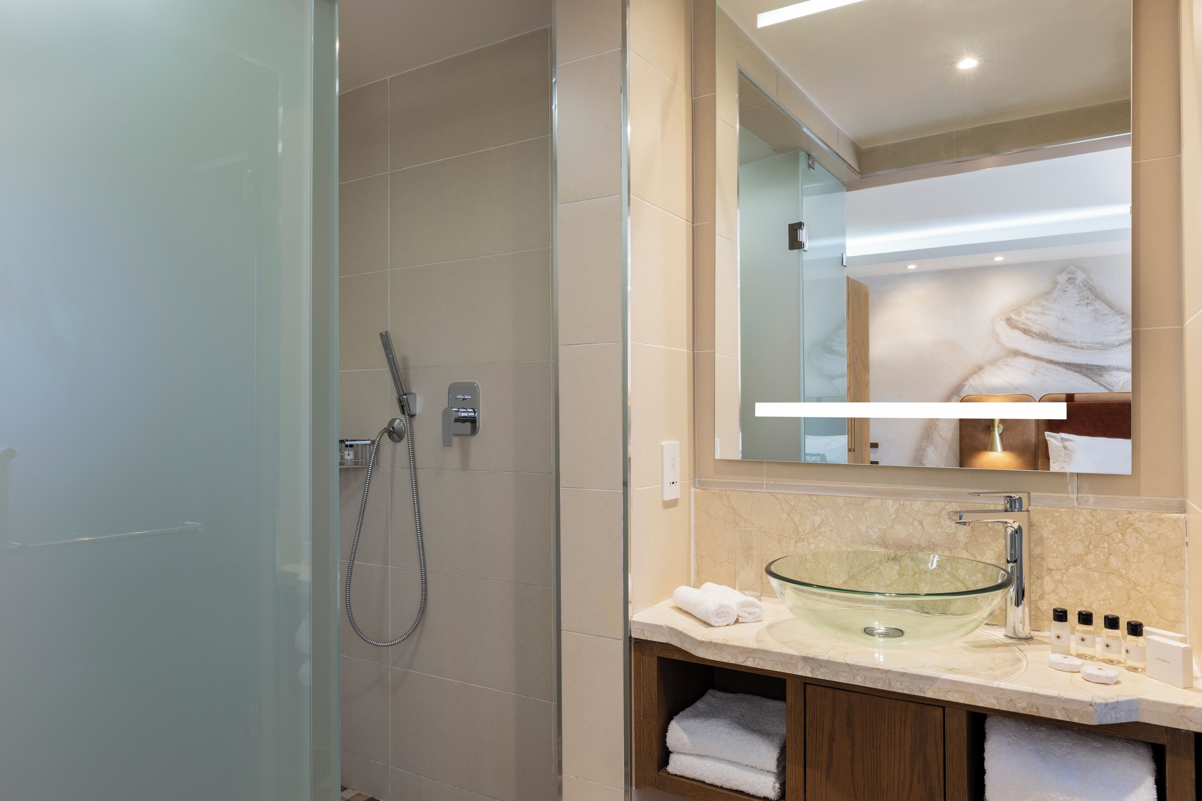 A modern bathroom with a glass vessel sink, a shower enclosure, and a mirror above the sink.