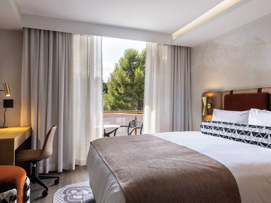 Habitación de hotel con cama, escritorio, silla y vistas al exterior.