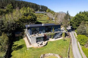 A modern two-story house with a stone foundation, large windows, and a covered outdoor seating area. - Luxury Mansion in Dublin 18 (Kilgobbin)