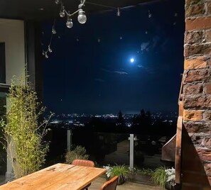 An outdoor patio with a wooden table and chairs, a hanging light fixture, and a view of the cityscape at night. - Luxury Mansion in Dublin 18 (Kilgobbin)