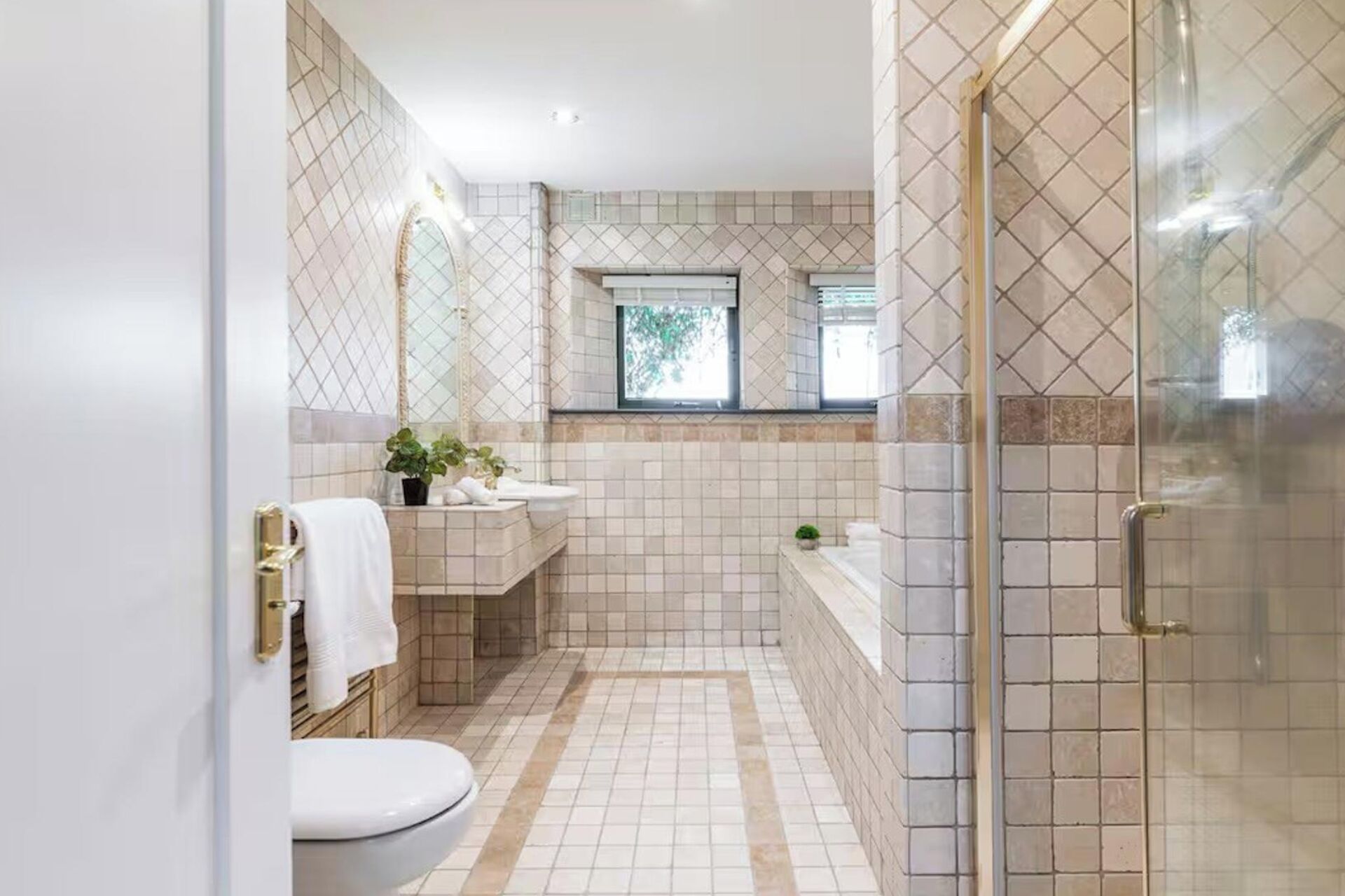 Un baño con inodoro, lavamanos y zona de ducha, con piso y paredes de azulejos.