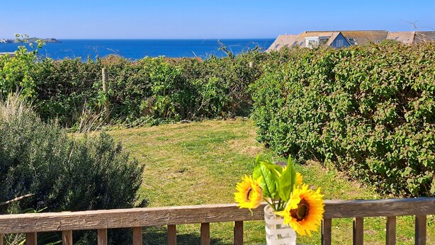 Een tuin met een houten omheining, een houten terras en uitzicht op zee.