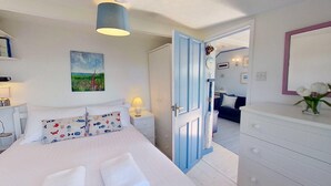 Een slaapkamer met een bed, nachtkastjes, een dressoir, een spiegel en een deur naar een andere kamer.
