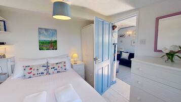 Een slaapkamer met een bed, nachtkastjes, een dressoir, een spiegel en een deur naar een andere kamer.