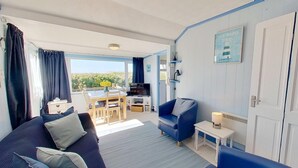 Een woonkamer met een blauwe bank, een televisie, een eettafel met stoelen en uitzicht op de omgeving.