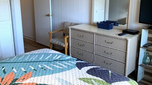 Ein Schlafzimmer mit Bett, Kommode, Stuhl, Spiegel und Fernseher.