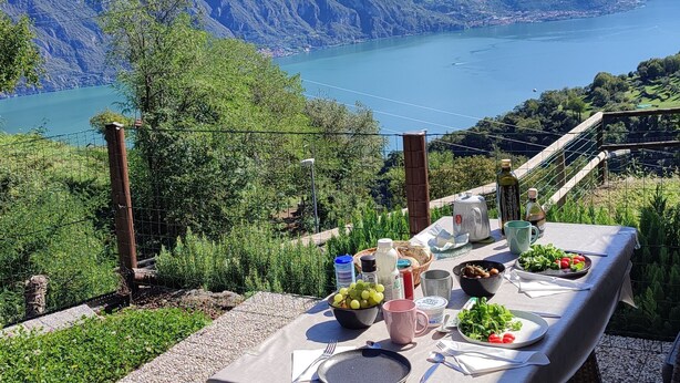 Ein Tisch, reichhaltig gedeckt mit Speisen und Getränken, mit Blick auf einen See vor einer Bergkulisse.