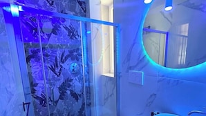 A modern bathroom with a glass shower enclosure, a marble sink, and a round mirror. - ESE luxury spa suites (Rome)