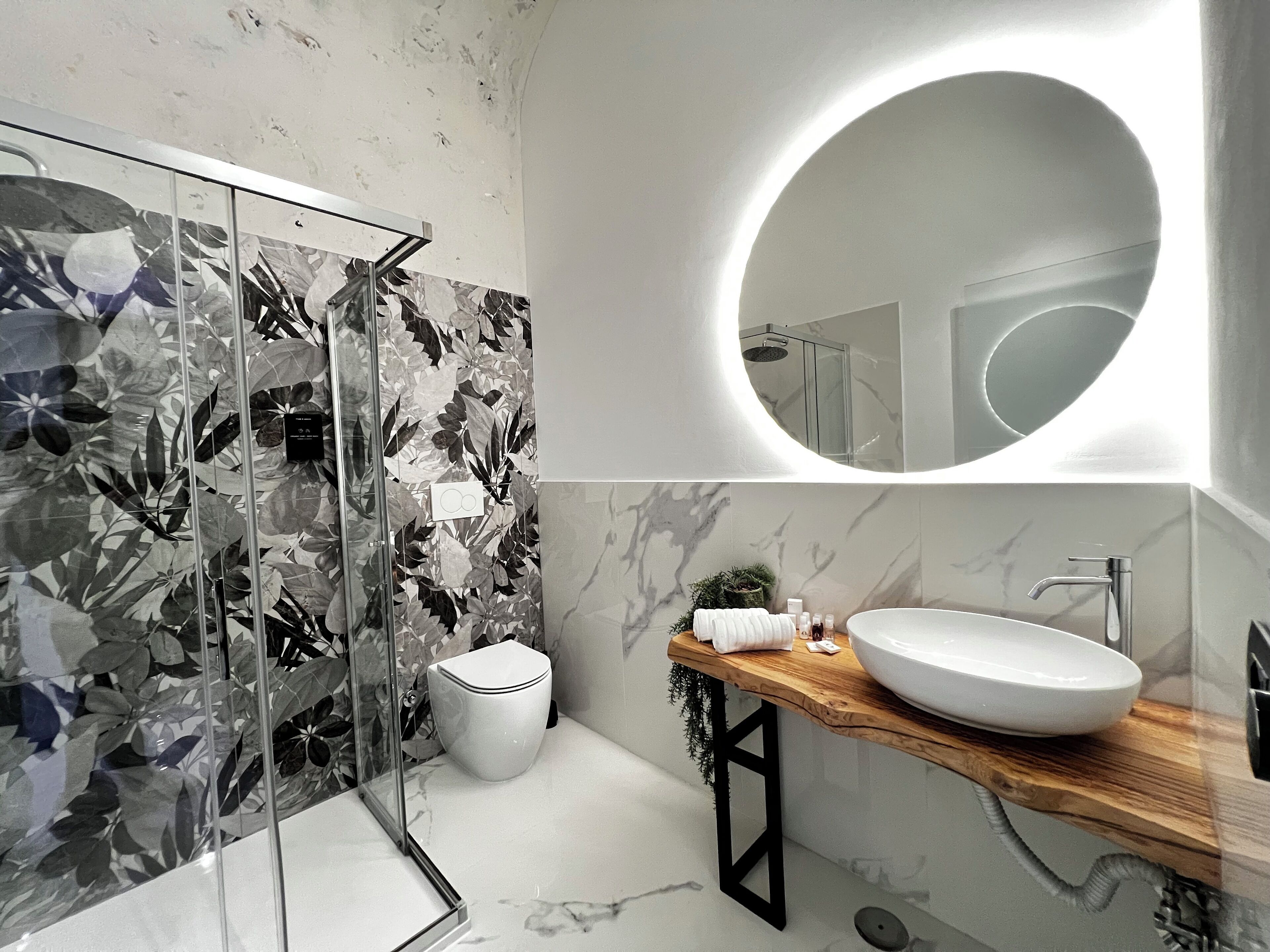 A modern bathroom with a glass shower enclosure, a toilet, a sink with a wooden countertop, and a large mirror.