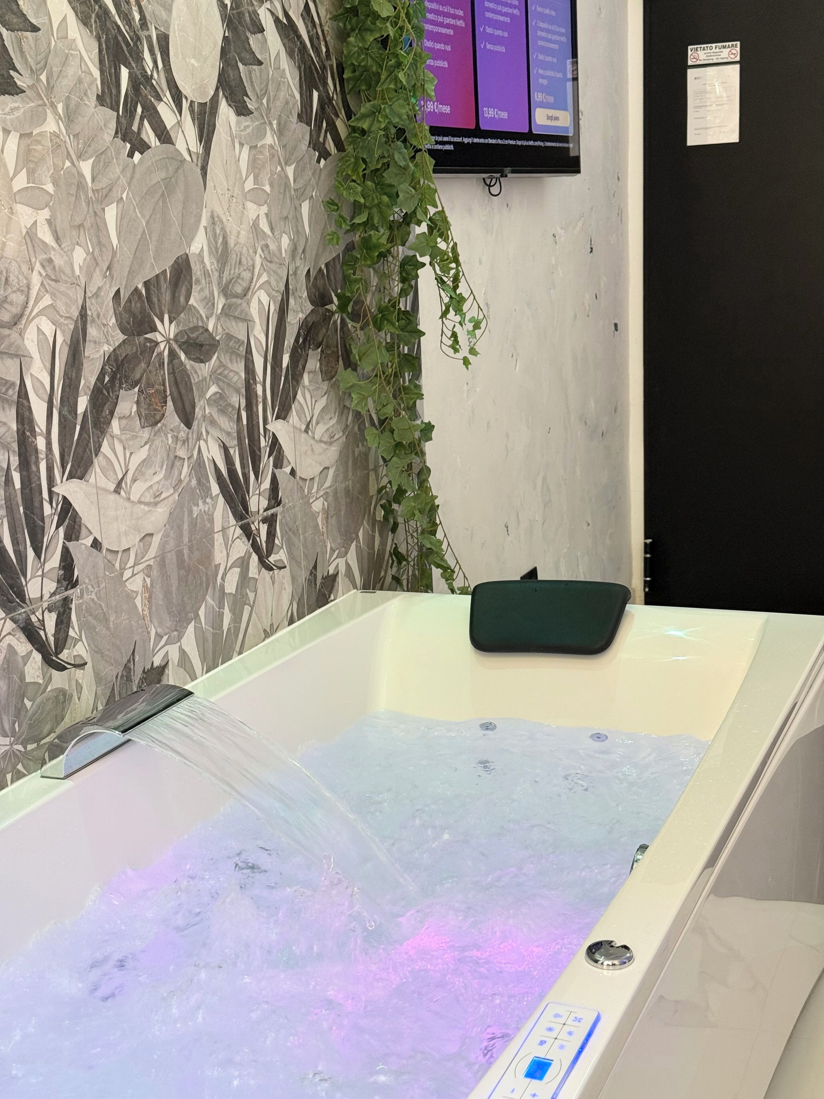 A bathtub with a control panel, a wall-mounted TV, and a door with a sign.