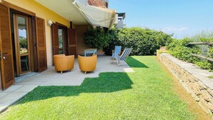 A modern outdoor patio with a yellow wall, wooden shutters, and a covered seating area. - Charming Porto Santo Stefano Apartment With Pool Access (Monte Argentario)