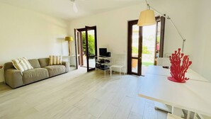 A spacious living area with a sofa, a TV, and a dining table. - Charming Porto Santo Stefano Apartment With Pool Access (Monte Argentario)