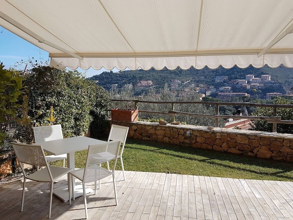 An outdoor patio with a table and chairs, a stone wall, and a view of a hillside town.